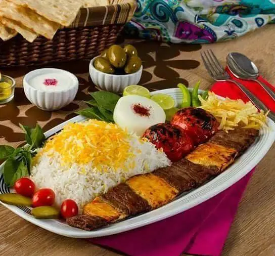 یک بشقاب چلو کباب لذیذ رستوران سلطان شامل برنج زعفرانی، کباب، گوجه کبابی، زیتون و ماست. بهترین غذای ایرانی.