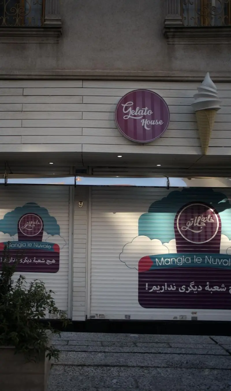 ژلاتو هاوس: نمای مغازه بستنی فروشی با تابلوی Gelato House، مجسمه بستنی قیفی بزرگ، کرکره‌های طرح ابر و پیام "هیچ شعبه دیگری نداریم".