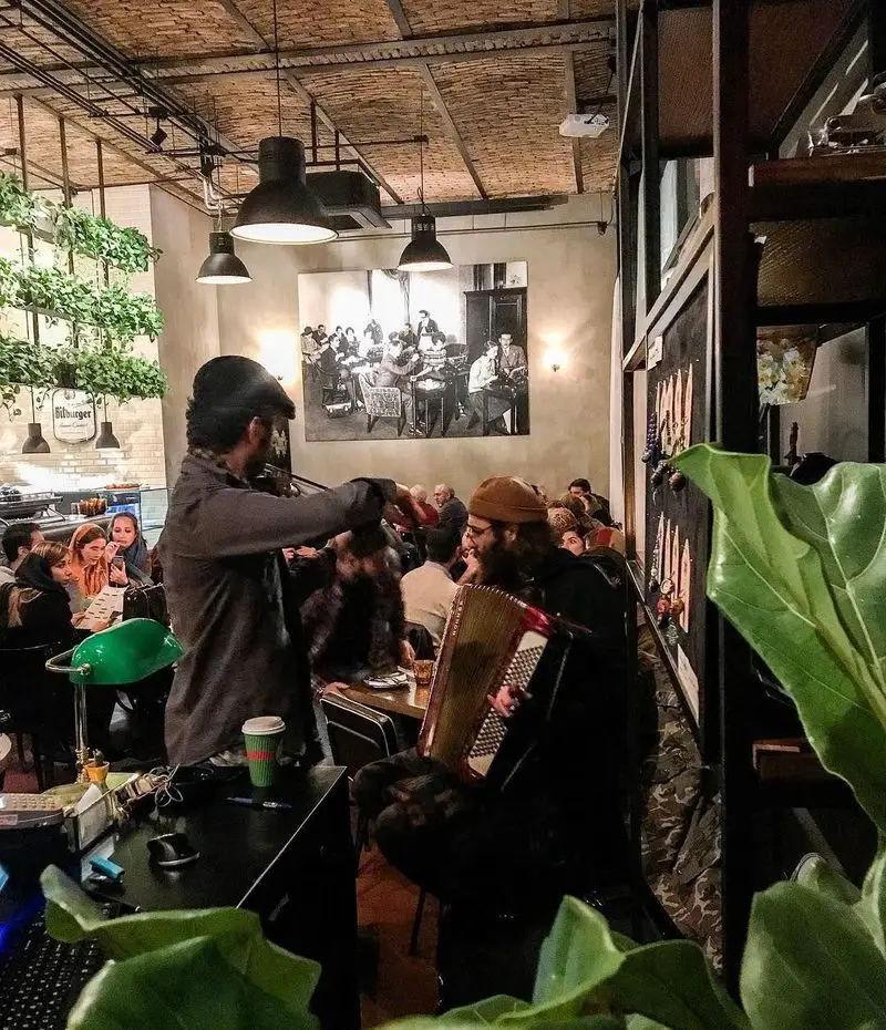 نمایی دلنشین از کافه تایپ با موسیقی زنده ویولن و آکاردئون. مشتریان در فضای گرم و هنری کافه دور هم جمع شده‌اند.