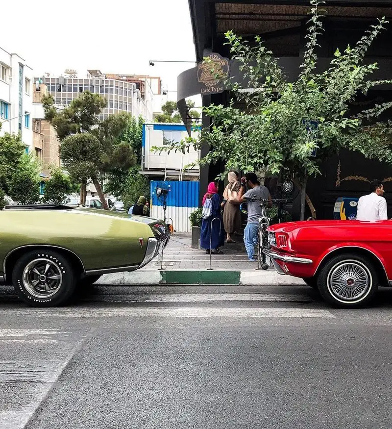 کافه تایپ در یک روز دلپذیر با حضور ماشین‌های کلاسیک سبز و قرمز در خیابان، مشتریان در فضای باز و دنج کافه از نوشیدنی لذت می‌برند.