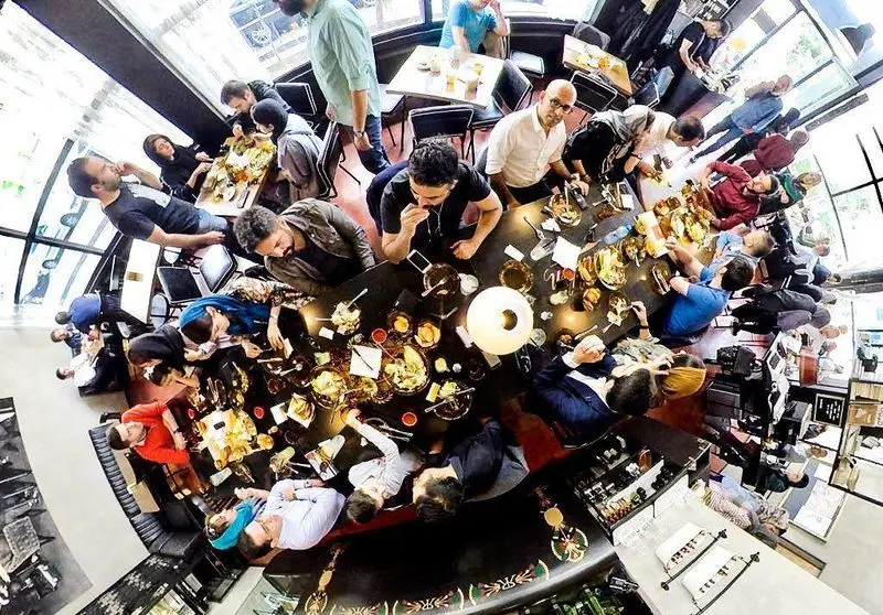 محیط گرم و دلنشین کافه تایپ با مشتریان شاد در حال لذت بردن از انواع غذا و نوشیدنی‌های خوشمزه در فضایی دنج و دوستانه.