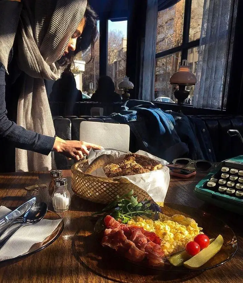 فضایی دلنشین و دنج در کافه تایپ: صبحانه کامل با املت، بیکن، نان تازه و دستگاه تایپ قدیمی کنار پنجره آفتابی.