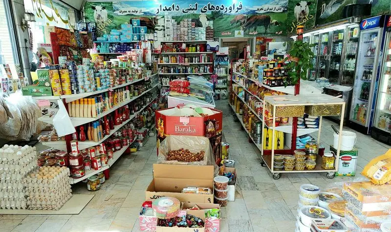 تصویری کامل از فروشگاه سوپر لبنیاتی دامدار، نمایش انواع فرآورده‌های لبنی، تخم مرغ، کنسرو، سس و خشکبار در قفسه‌های منظم و پر.