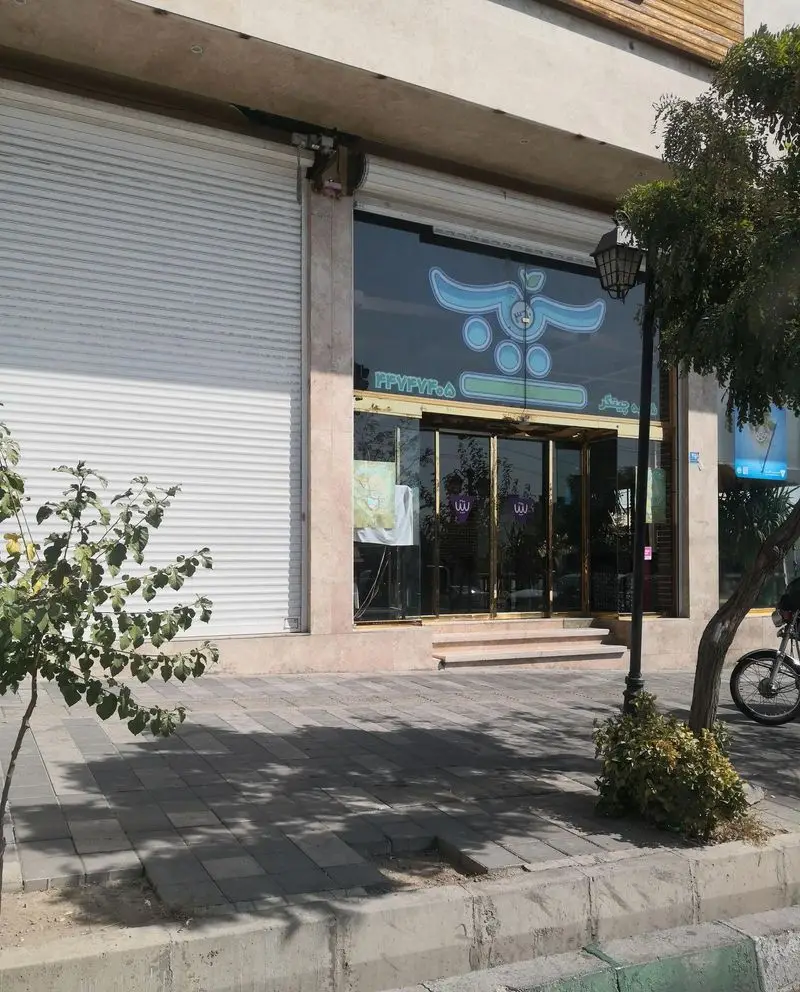 تصویر بیرونی فست فود پیتزا سیب ۳۶۰ شعبه چیتگر با لوگوی بزرگ آبی روی شیشه و ورودی طلایی، شامل کرکره کنار آن.