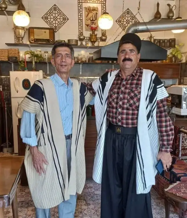 کافه فرش: دو مرد در لباس‌های سنتی ایرانی در فضای دکوراسیون اصیل کافه فرش، تجربه دلنشین فرهنگ و هنر ایرانی.