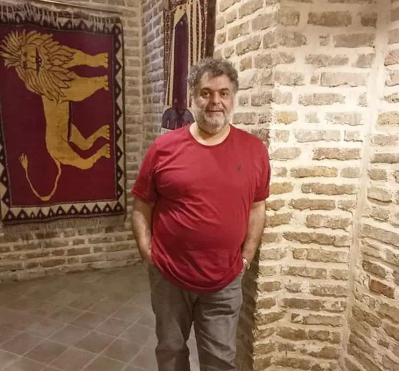 مردی در کافه فرش، فضایی دلنشین با دکوراسیون سنتی و دیوارهای آجری. تابلو فرش نفیس با طرح شیر، جلوه‌ای از هنر اصیل ایرانی.