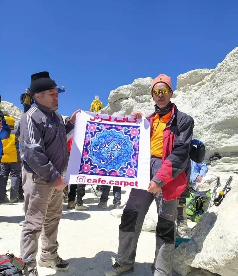 تصویری از کوهنوردانی که در طبیعتی کوهستانی، بنر کافه فرش را با لوگوی زیبا و نام تجاری cafe.carpet به نمایش گذاشته‌اند.