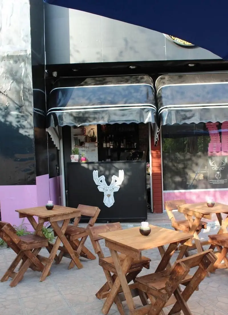 نمای بیرونی کافه فست فود ویچنزا با میز و صندلی‌های چوبی در فضای باز، همراه با لوگوی گوزن روی پیشخوان و سایبان‌های مشکی.