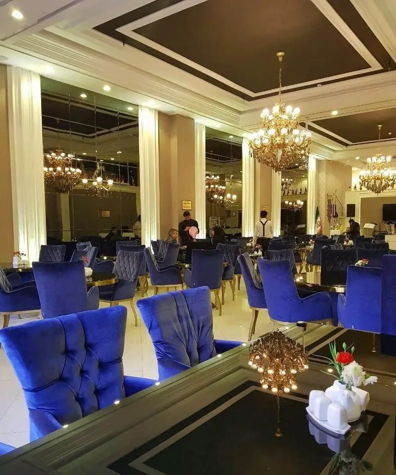 نمای داخلی مجلل رستوران فرنگی حافظ با صندلی‌های مخملی آبی، میزهای شیک، لوسترهای طلایی و آینه‌کاری دیوارها.