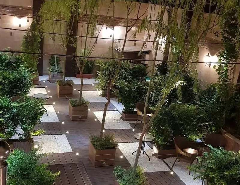 فضای باز دلنشین و سرسبز رستوران فرنگی حافظ در شب با نورپردازی زیبا، میز و صندلی‌ها بین درختان، مناسب دورهمی.