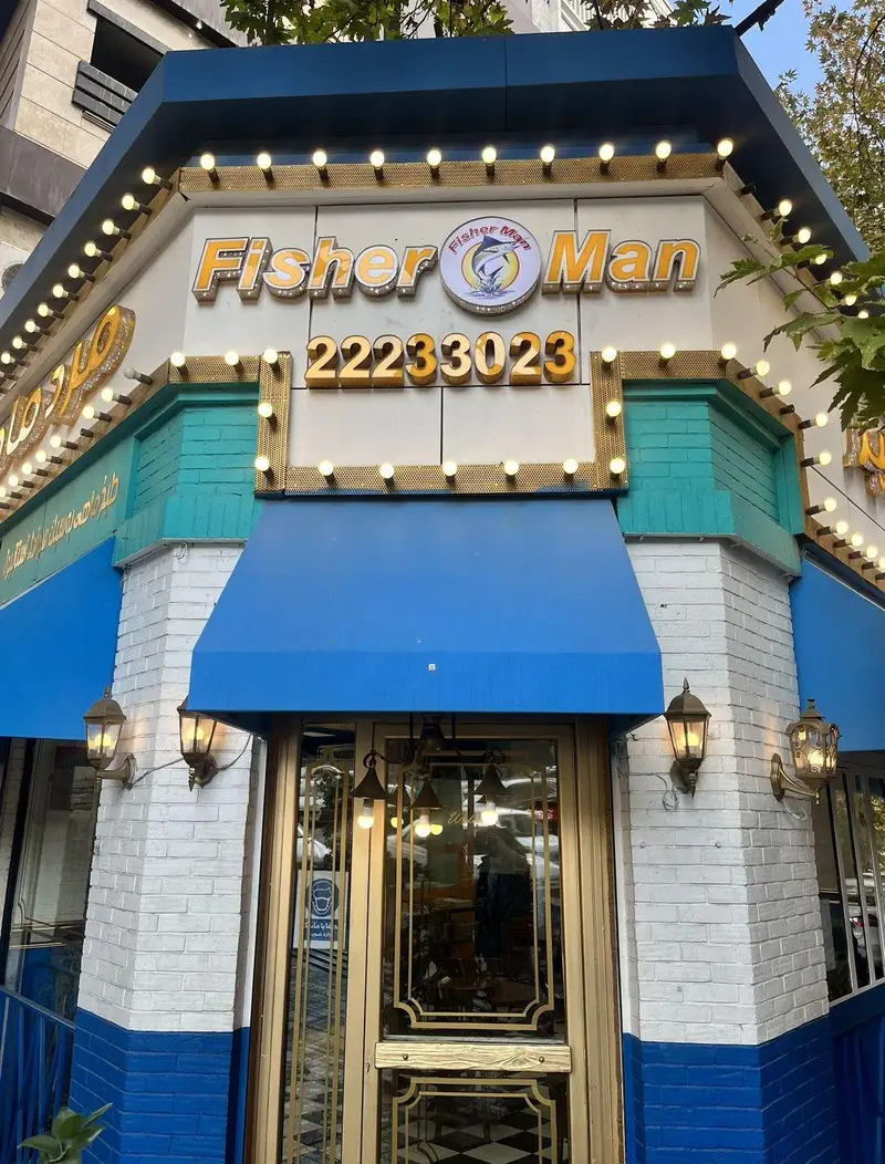 تصویری از نمای بیرونی رستوران دریایی فیشر من (مرد ماهی‌گیر) شعبه اندرزگو با تابلو روشن، سردر آبی و آجر سفید
