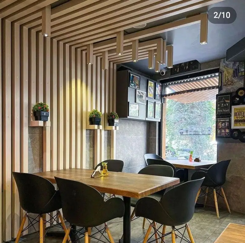 نمایی از دکوراسیون داخلی مدرن و دنج کافه کلاور با دیوارها و سقف چوبی، میز و صندلی‌های شیک و نورپردازی جذاب.