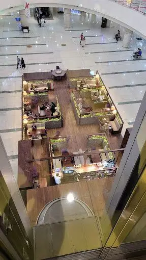 تصویری از داخل مگا مال، نمایش دهنده طبقه وسیع و مدرن با کافه و رستوران شیک، و افراد در حال خرید و تردد در مرکز خرید.