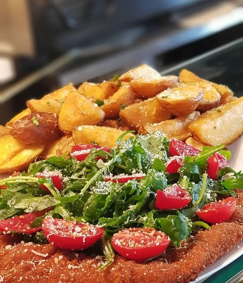 میلانزه یا شنیتسل خوشمزه به همراه سیب زمینی تنوری و سالاد روکا و گوجه گیلاسی در رستوران ایتالیایی بونو ظفر، بهترین غذای اصلی.