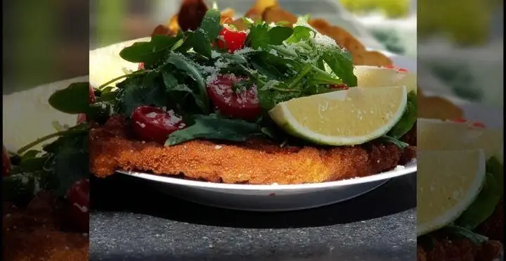 شنیسل ترد و لذیذ با روکولا تازه، گوجه گیلاسی، پنیر پارمزان رنده شده و برش لیمو در رستوران ایتالیایی بونو ظفر. طعم اصیل غذای ایتالیایی.