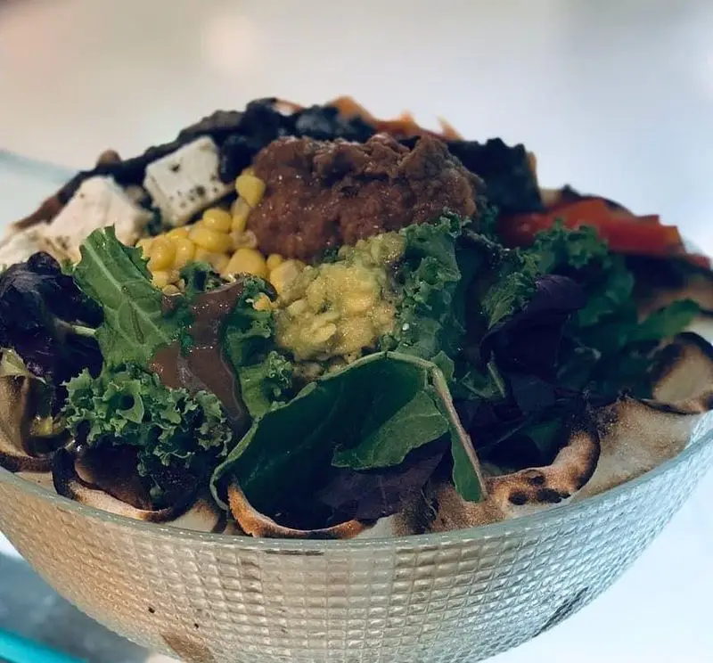 کاسه سالاد سالم و خوشمزه در رستوران ایتالیایی بونو ظفر، حاوی سبزیجات تازه، ذرت، تکه‌های پنیر، سس قهوه‌ای و نان تُست دور کاسه.