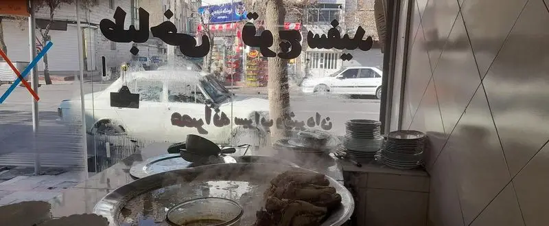 فضای داخلی طباخی قوچ سفید: کله پاچه بخارپز و داغ در ظروف بزرگ، آماده سرو. بازتاب خیابان و خودروها در شیشه مغازه.