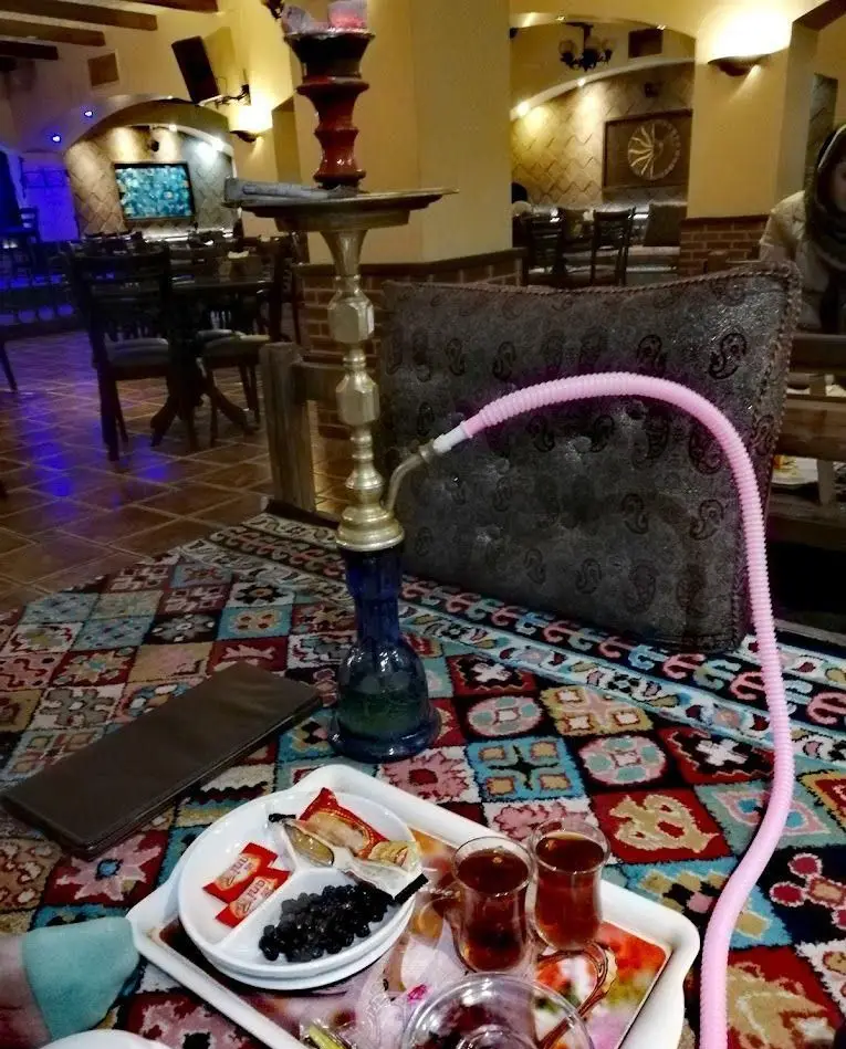 فضای داخلی رستوران سنتی و سفره خانه عمارت، شامل قلیان، سینی چای و خوراکی روی فرش اصیل ایرانی با دکوراسیون دلنشین.