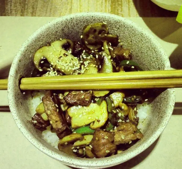 غذای آسیایی لذیذ در رستوران فرنگی پیچ: بیف و قارچ با برنج و کنجد، سرو شده با چاپستیک. تجربه غذایی بی‌نظیر.