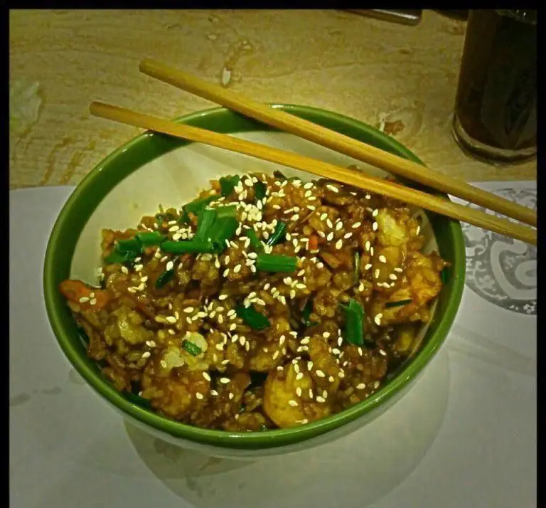 یک کاسه برنج سرخ شده خوشمزه با میگو، پیازچه و کنجد، همراه با چاپستیک در رستوران فرنگی پیچ. غذایی لذیذ برای تجربه.