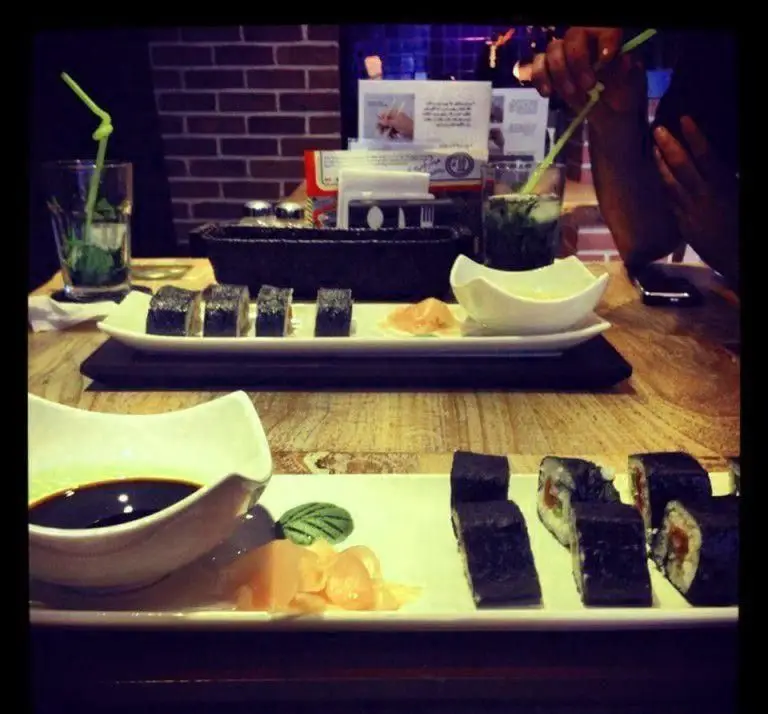 میز رستوران فرنگی پیچ با رول‌های سوشی و ماکی، سس سویا و زنجبیل، همراه با نوشیدنی گوارا در فضایی دلنشین.