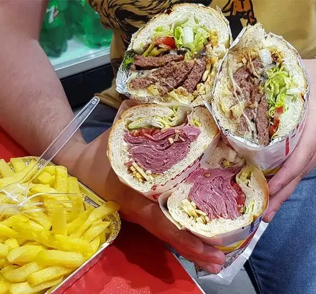 تصویری جذاب از چهار ساندویچ بزرگ و لذیذ ساندویچ هایدا ستارخان، شامل ساندویچ های ژامبون و گوشت، همراه سیب زمینی سرخ کرده.