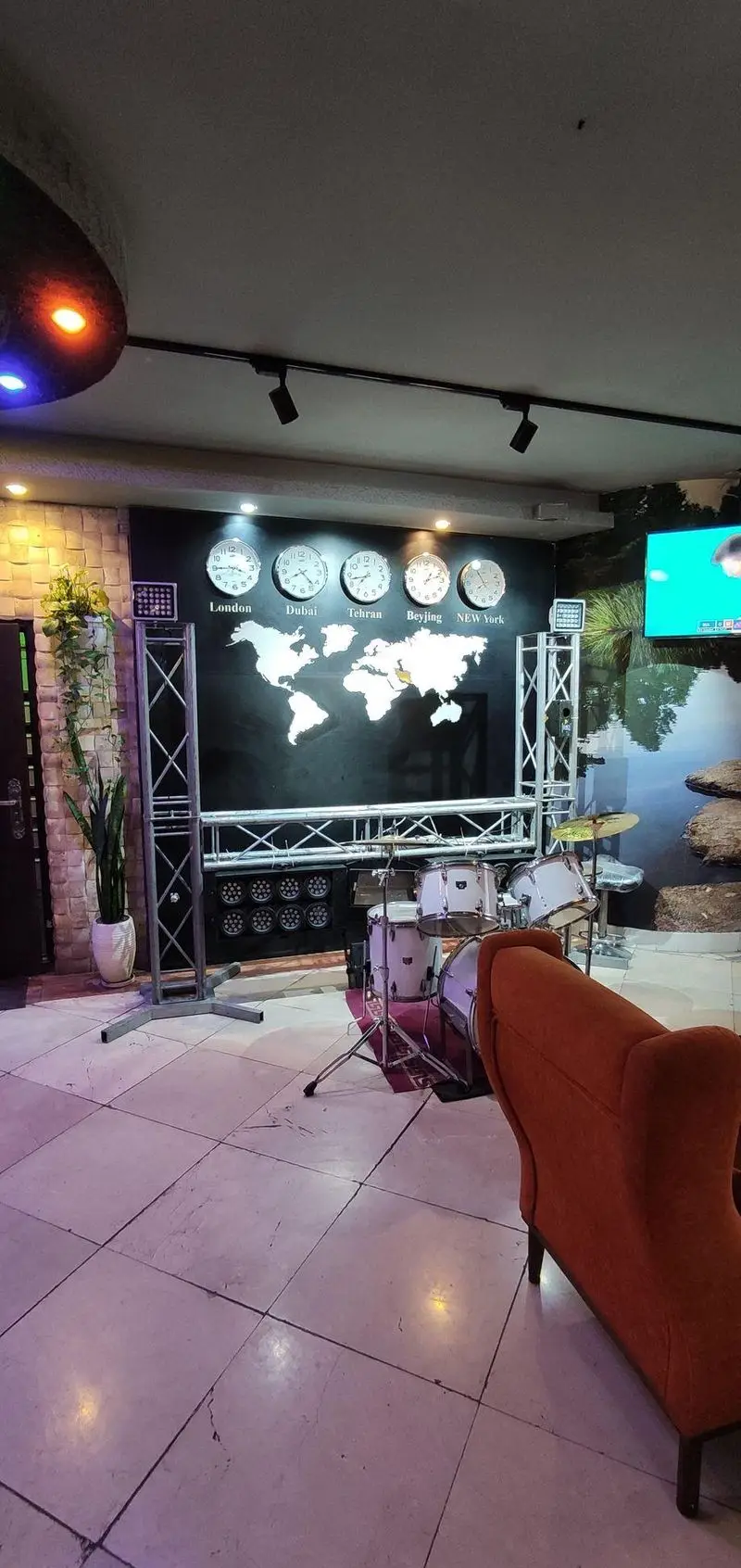 کافه رستوران سالار: نمایی از فضای داخلی با استیج درام، نقشه جهان و ساعت‌های جهانی، نورپردازی خاص و مبلمان راحت.