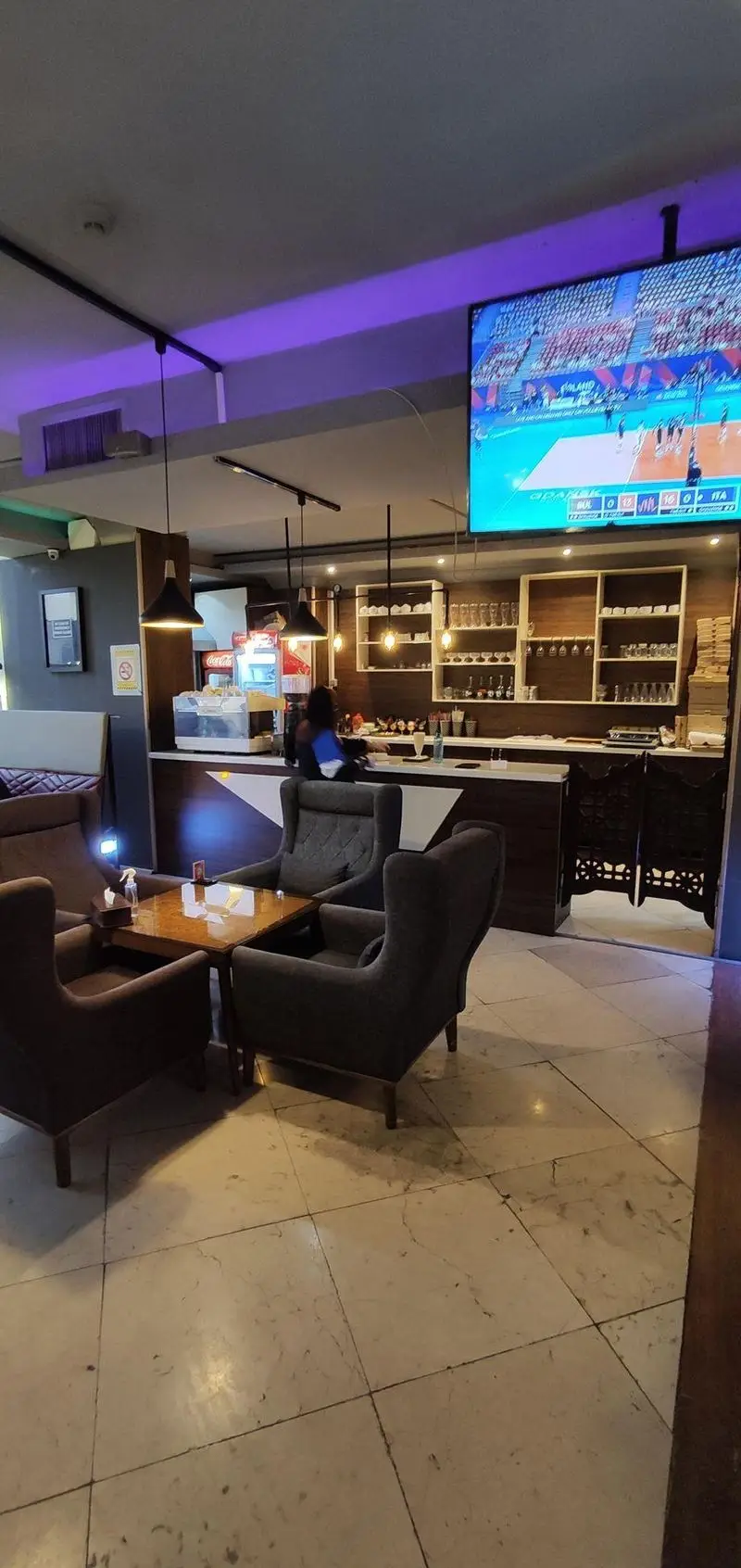 فضای داخلی کافه رستوران سالار: دکوراسیون مدرن، صندلی‌های راحتی، میزهای چوبی، بار کامل نوشیدنی، تلویزیون بزرگ ورزشی و نورپردازی دلنشین.