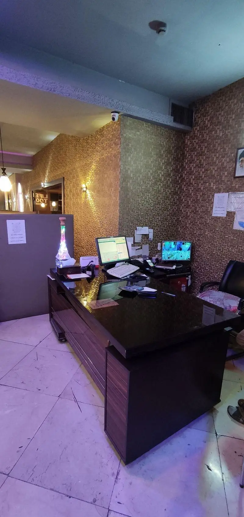 فضای داخلی کافه رستوران سالار: میز پذیرش مدرن با سیستم‌های کامپیوتری، دیوارهای طرح‌دار طلایی و سقف آبی. دوربین امنیتی نیز دیده می‌شود.