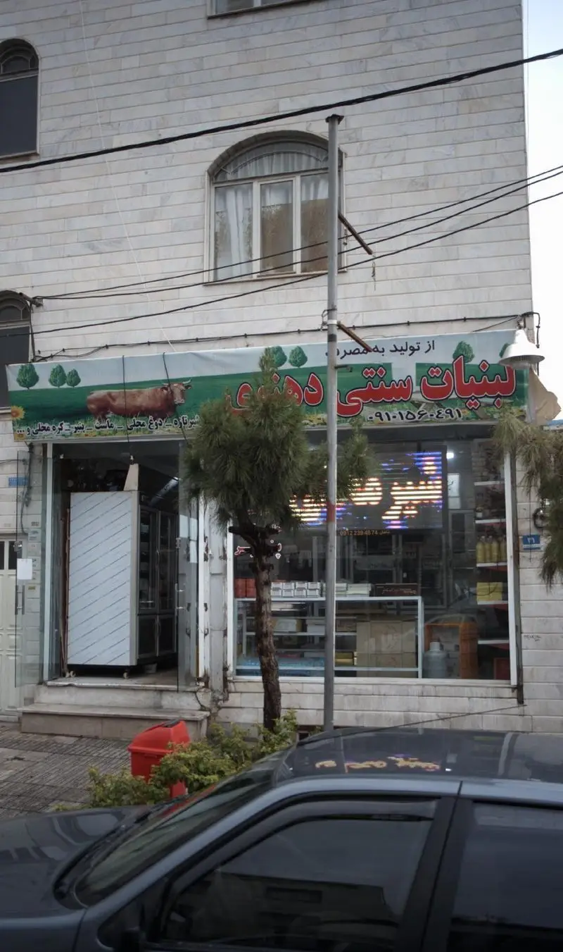 نمای بیرونی یک مغازه لبنیات سنتی یزدی در ایران، با تابلوی بزرگ و عکس گاو، عرضه کننده محصولات تازه لبنی مانند شیر، ماست و پنیر محلی.