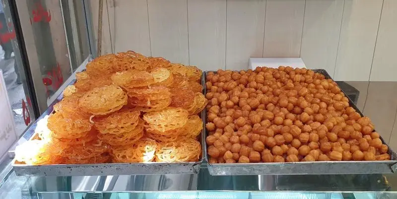 سینی‌های پر از زولبیا و بامیه طلایی و آبدار، شیرینی‌های سنتی پرطرفدار ایرانی در قنادی فرح بخش، آماده سرو.