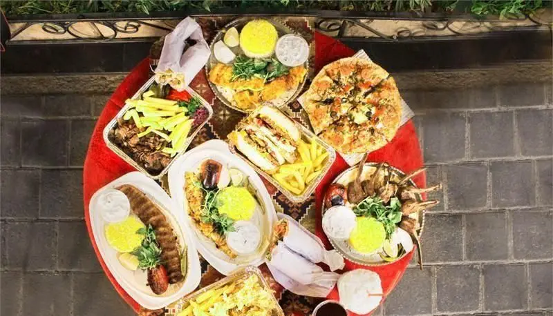 میز بزرگ و قرمز رنگ پر از انواع غذاهای لذیذ فست فود مجموعه آرمن از جمله کباب، پیتزا، ساندویچ، ماهی و سیب زمینی سرخ کرده.