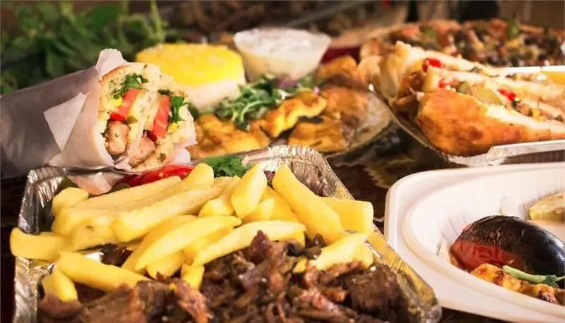 تصویر میز مملو از غذاهای لذیذ و متنوع فست فود مجموعه آرمن، شامل ساندویچ، انواع کباب، سیب زمینی سرخ کرده و برنج زعفرانی.