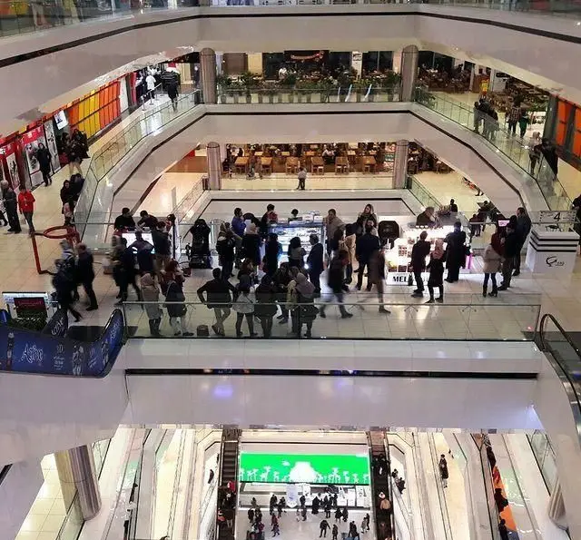 نمای داخلی شلوغ و چندطبقه یک مرکز خرید مدرن، پر از مشتریان و فضاهای غذاخوری در سطوح مختلف. فست فود پوآچا بخشی از این محیط پر جنب و جوش.