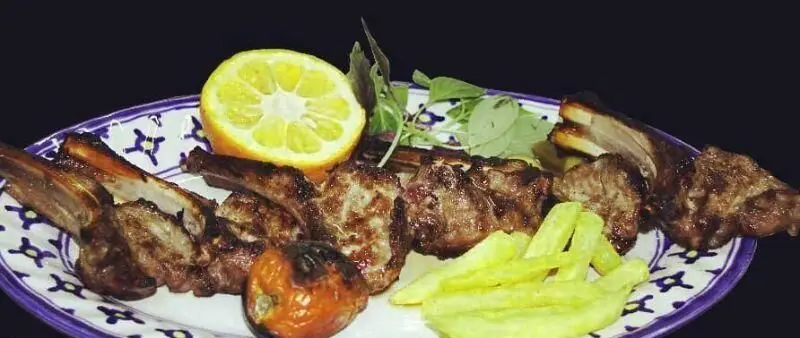 دنده کباب لذیذ سفره خانه سنتی باربد، با لیمو، سیب زمینی سرخ کرده، گوجه کبابی و سبزی تازه در بشقاب سنتی.