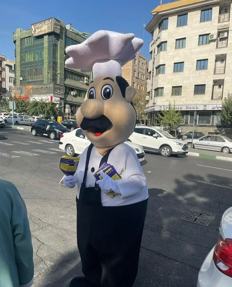 ماسکوت جذاب سرآشپز تهیه غذای ستاره ایلیا در حال توزیع بروشورهای تبلیغاتی در خیابان شلوغ شهر تهران.