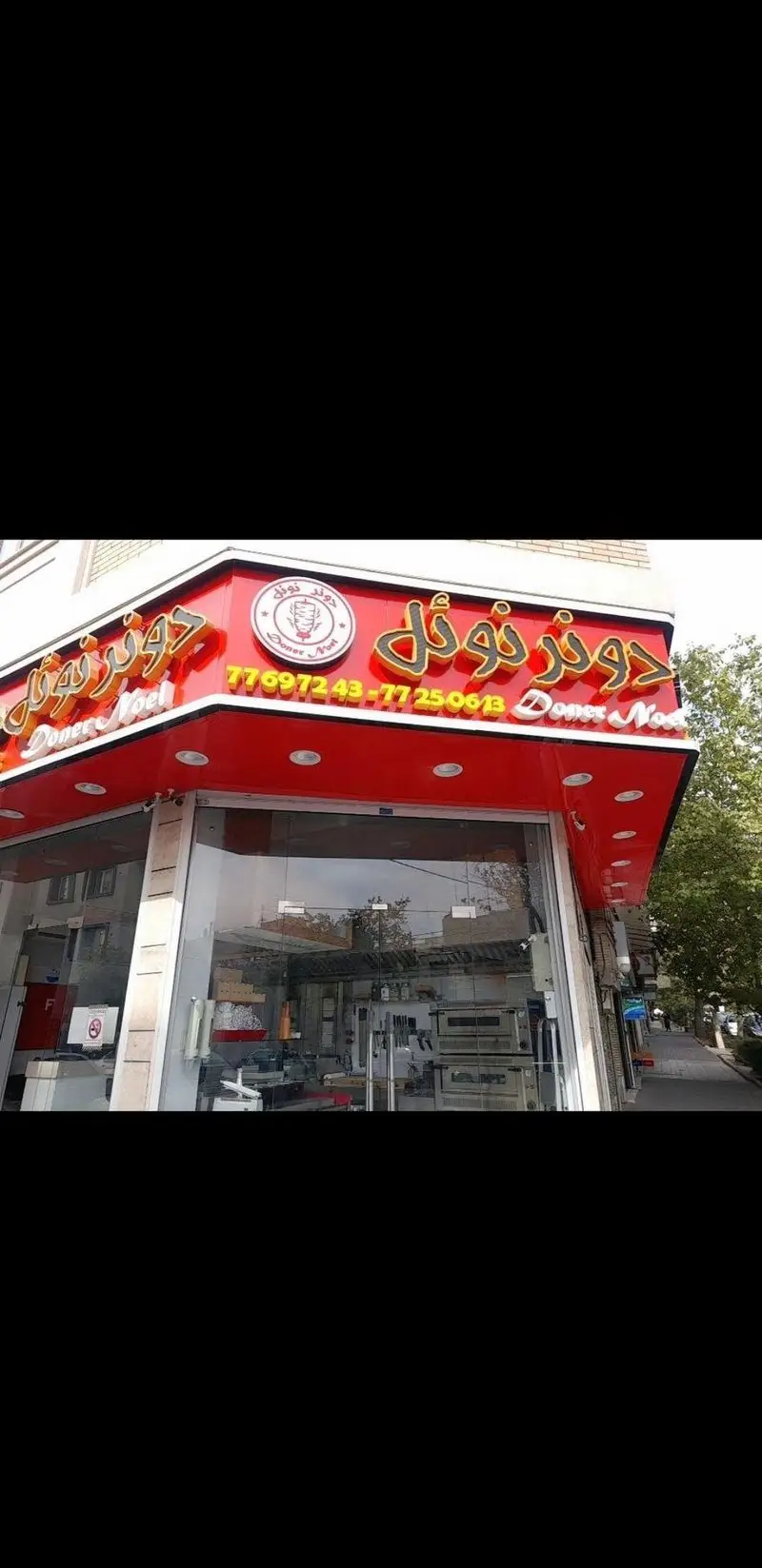 نمای بیرونی و تابلوی درخشان فست فود دونر نوئل با فونت طلایی و لوگوی دونر کباب، همراه با شماره‌های تماس ۷۷۶۹۷۲۴۳ و ۷۷۲۵۰۶۱۳.