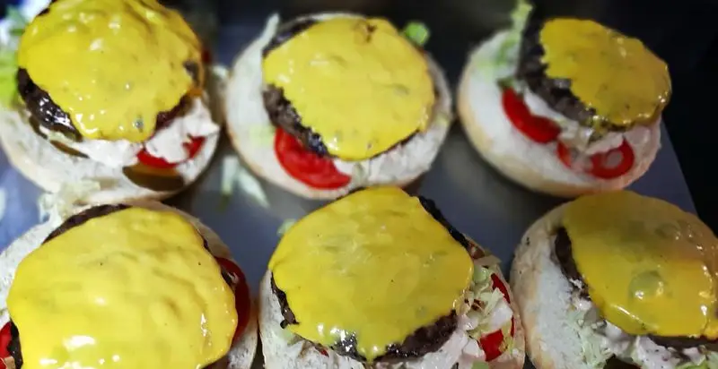 شش همبرگر ذغالی خوشمزه از باروشه با سس پنیر طلایی، کاهو و گوجه فرنگی روی نان تازه، آماده برای سرو.