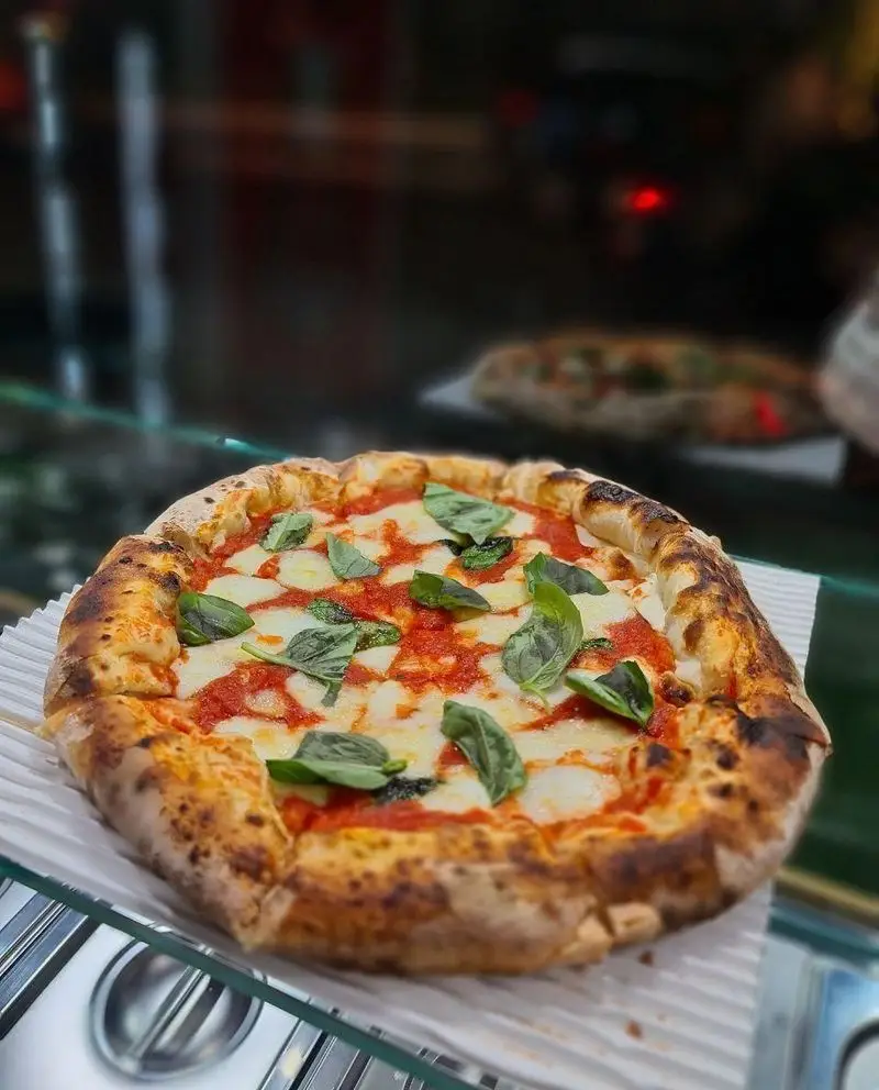 پیتزا مارگاریتا ناپولی تازه و خوشمزه از پیتزا آمی چی با پنیر موزارلا ذوب شده، سس گوجه فرنگی غنی و برگ‌های ریحان سبز روشن.