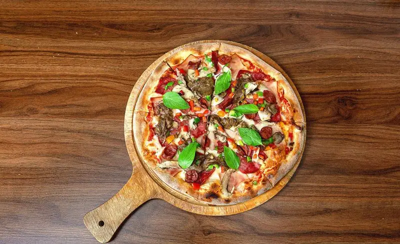 پیتزا مخصوص آمی چی با تاپینگ‌های گوشت، پپرونی، قارچ و سبزیجات تازه، روی تخته چوبی. تجربه‌ای خوشمزه از غذای ایتالیایی.