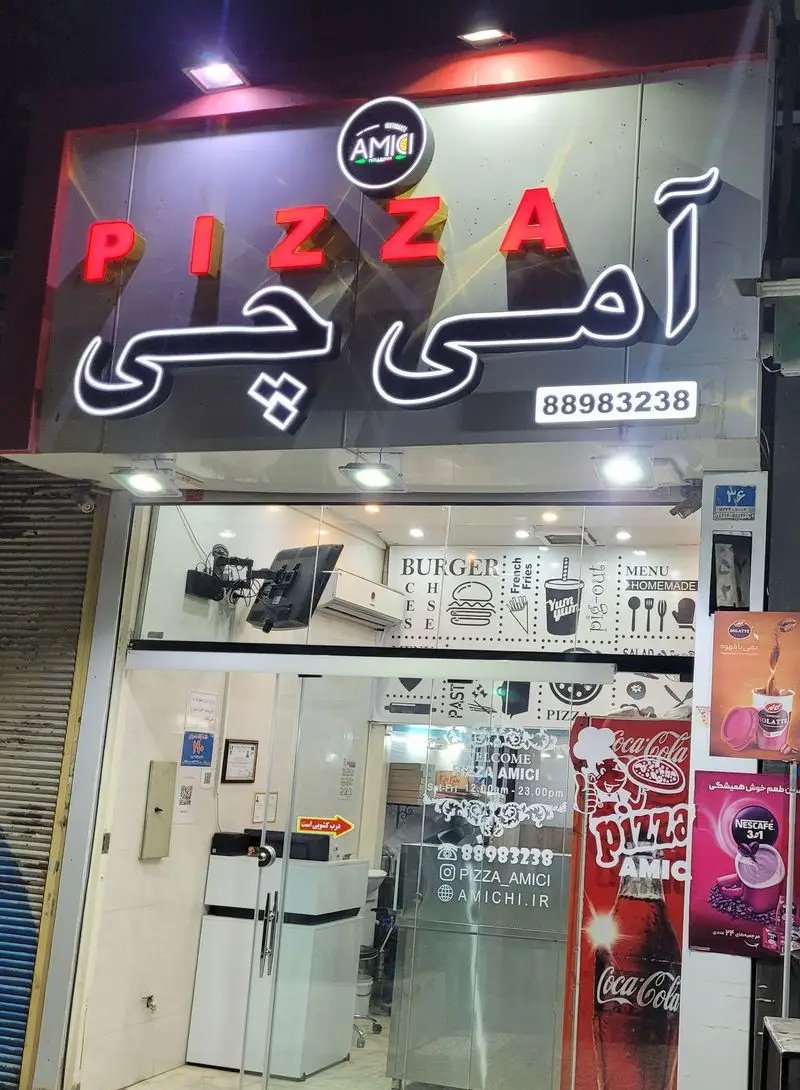 تصویر نمای بیرونی پیتزا آمی‌چی: تابلوی روشن، منوی کامل پیتزا، برگر و فست فود، با شماره تماس 88983238 و آدرس AMICHI.IR.