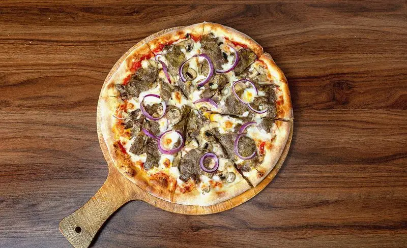 پیتزا گوشت و قارچ لذیذ پیتزا آمی چی، با پیاز قرمز تازه، روی تخته چوبی سرو شده. بهترین انتخاب برای سفارش آنلاین و تحویل سریع.