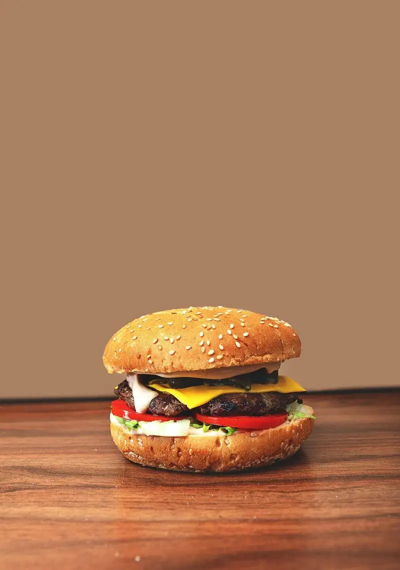 عکس نزدیک از یک چیزبرگر لذیذ پیتزا آمی چی با نان کنجدی، دو لایه گوشت، پنیر آب شده، گوجه، کاهو و سس مخصوص.