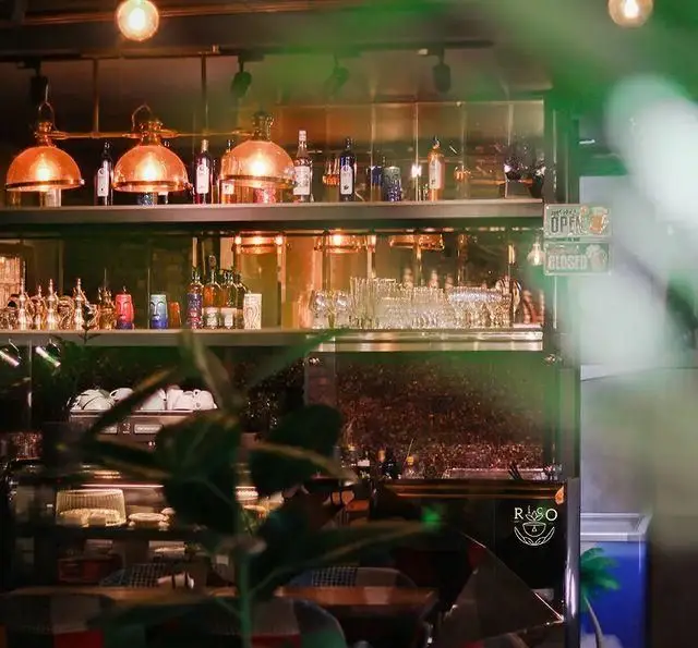 فضای داخلی جذاب کافه ریکو با قفسه‌های شیک نوشیدنی، لیوان‌های مرتب و ظروف قهوه. نورپردازی گرم، محیطی دلپذیر ایجاد کرده است.