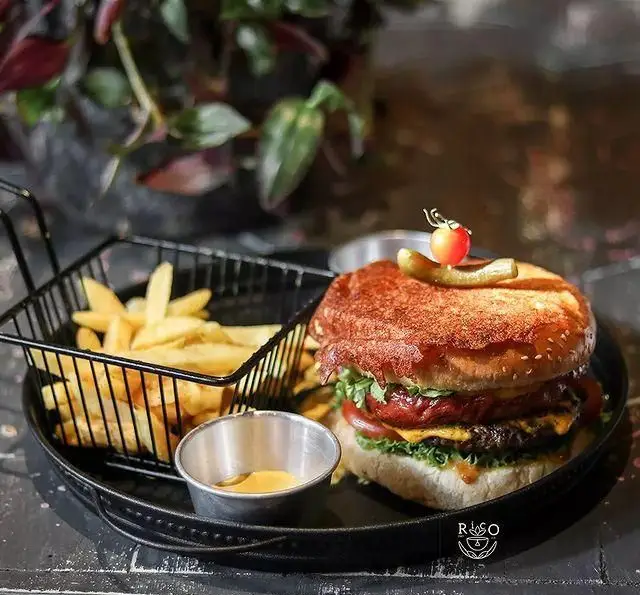 همبرگر دوبل پتی کافه ریکو با پنیر، کاهو و گوجه فرنگی، همراه سیب زمینی سرخ کرده طلایی و سس دیپ، سرو شده در سینی مشکی.
