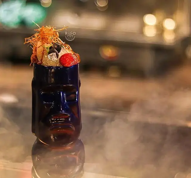 نوشیدنی منحصر به فرد کافه ریکو: کوکتل یا دسر خاص در ماگ تیکی آبی رنگ با تزئینات میوه تازه، شکر رشته‌ای و دیزاین خلاقانه.