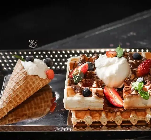 وافل‌های لذیذ کافه ریکو با سس شکلات، بستنی و میوه‌های تازه مانند توت فرنگی و بلوبری، در کنار بستنی قیفی، دسری خاص و جذاب.