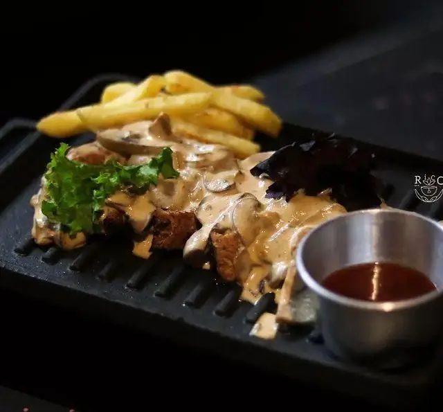 استیک یا مرغ با سس قارچ و سیب زمینی سرخ کرده کافه ریکو، سرو شده روی سینی چدنی همراه سس مخصوص و سبزیجات.