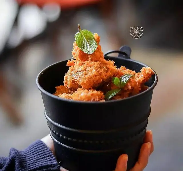 سطل مشکی کافه ریکو حاوی مرغ سوخاری ترد و طلایی با برگ‌های نعناع. غذای خوش‌رنگ و لذیذ برای تجربه فراموش‌نشدنی در کافه.