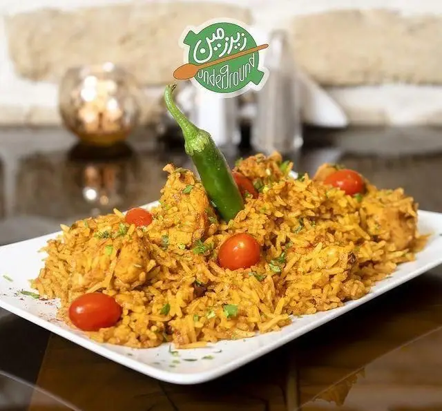 یک بشقاب بزرگ از بریانی مرغ خوشمزه و زعفرانی با گوجه گیلاسی و فلفل سبز در کافه رستوران زیرزمین سرو شده است.